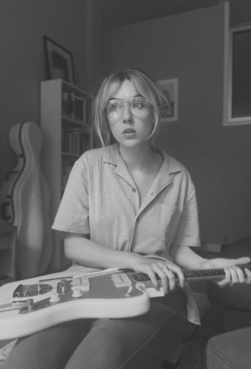 Black-and-white photo of Annie Koppes with her guitar, cello in the background