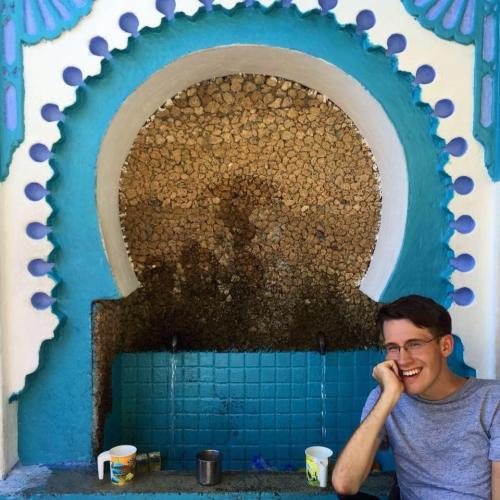 Bryan Rusch sits in front of a mosaic drinking fountain, smiling for the camera