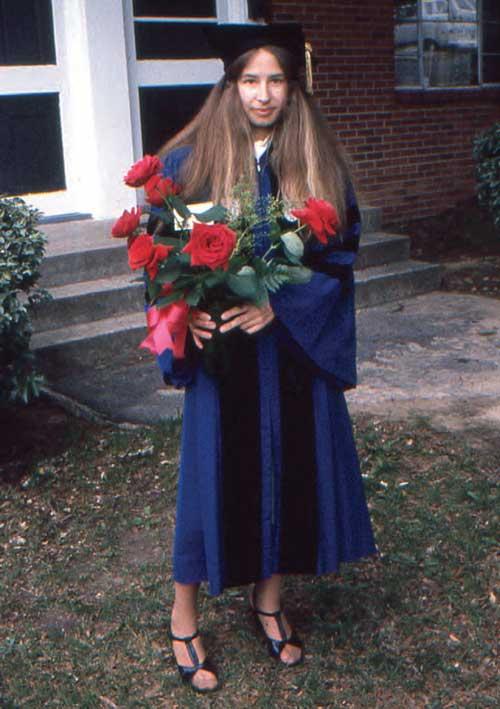 Dian Fox in her cap and gown holding a bouquet of red flowers.