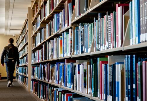 A photograph of the bookstacks in Perkins Library, with a student walking in between them.