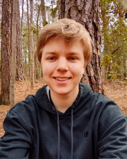 Headshot of Sam Brandsen in the woods, wearing a hoody