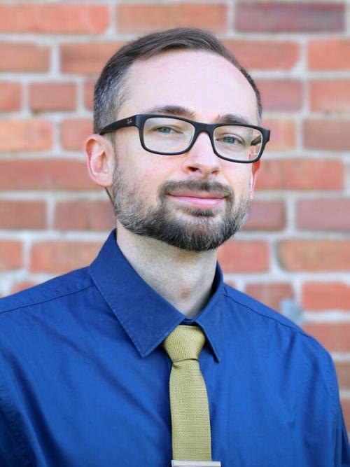 Professional headshot of Zachary Tumlin against a brick background