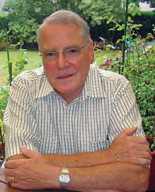 Michael Bassett posing with his arms crossed in front of a garden. 